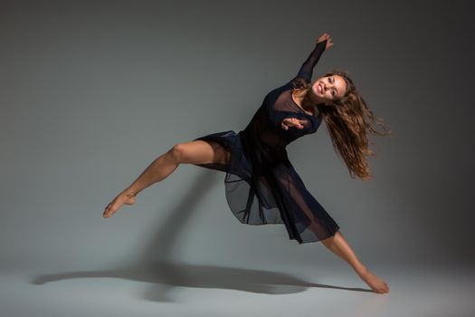 Dancing woman in a black dress. Contemporary modern dance on a gray background. Fitness, stretching model