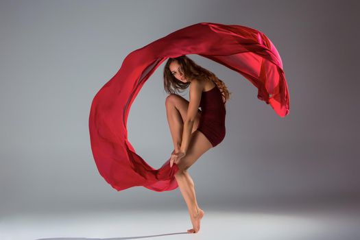 Young beautiful woman dancer in red swimsuit posing on a light grey studio background. Contemporary