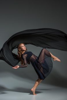 Dancing woman in a black dress. Contemporary modern dance on a gray background. Fitness, stretching model