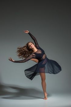 Dancing woman in a black dress. Contemporary modern dance on a gray background. Fitness, stretching model