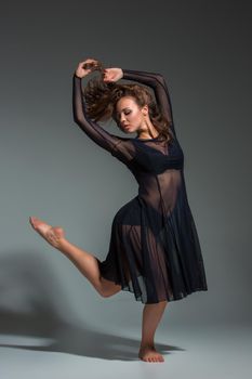 Dancing woman in a black dress. Contemporary modern dance on a gray background. Fitness, stretching model