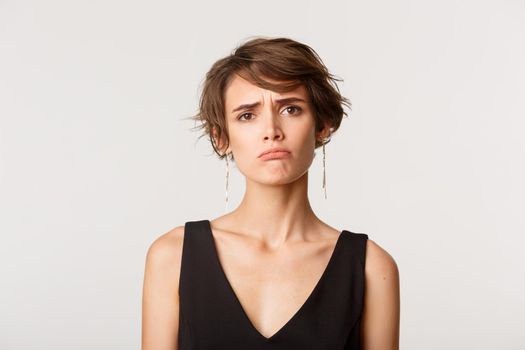 Close-up of distressed young gloomy woman frowning and pouting, standing over white background with sad face.