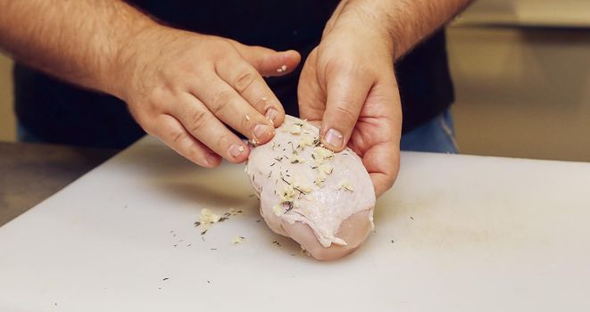 The cook sprinkled the chicken breast with salt. The hands of the cook rub the meat with spices.