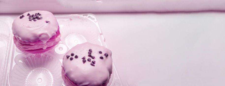 Two delicious donuts with icing sugar and chocolate chips in a transparent plastic container, a banner with a copy of the space on the right, pink tinting.