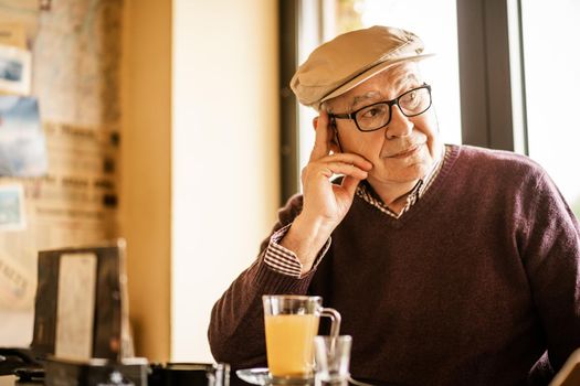 Senior man is sitting in cafe and drinking tea. He is pensive.