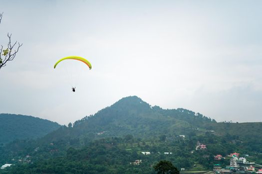 para gliding people with a bright orange yellow glider in the middle of hills mountains near nanital bir billing showing a popular adventure sport for tourists hill station