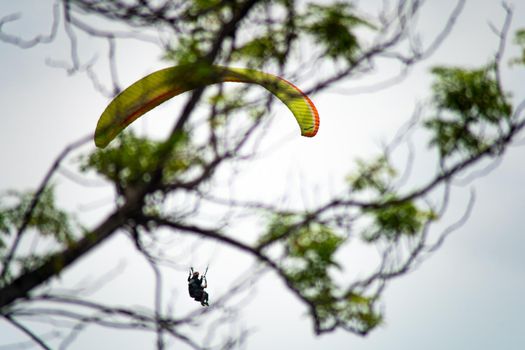 para gliding people with a bright orange yellow glider in the middle of hills mountains near nanital bir billing showing a popular adventure sport for tourists hill station