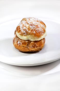 Focus on a cream puff and sugar on a porcelain plate