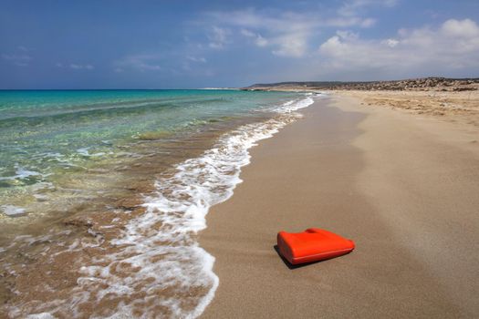 Bright red plastic oil (or washing liquid) container on beautiful unspoiled beach. Sea plastics littering concept. Karpazz, Northern Cyprus.