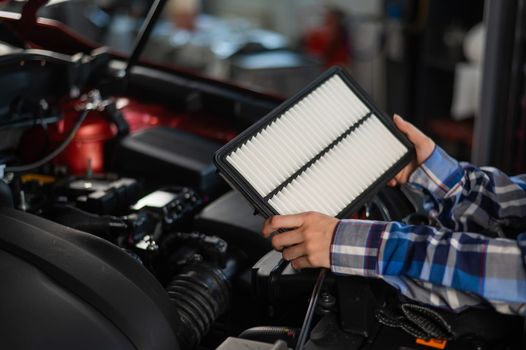 Caucasian female auto mechanic changes the engine air filter in the car