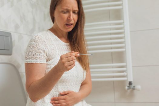 Worried middle age woman with pregnancy test in restroom