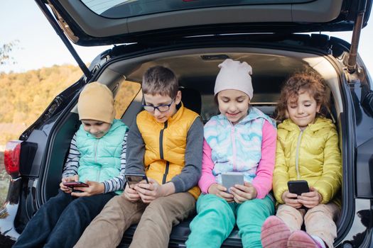 Children sitting on the car truck with smartphones and have fun