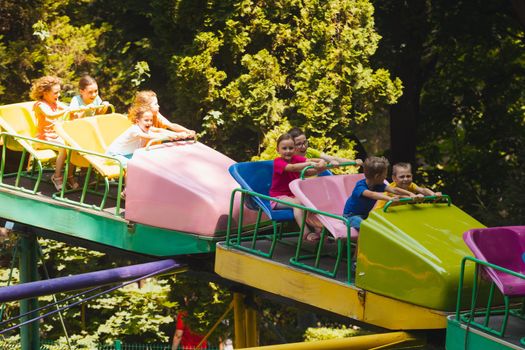 The happy little kids ride on a roller coaster in the amusement park on sunny day