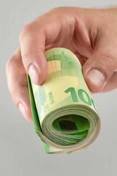 The hand holds a roll of 100 euro banknotes. Euro banknotes rolled up in a white man's hand on a gray background. The concept of financial assistance, real estate purchase, loan or insurance payment