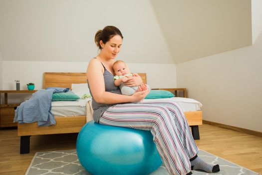 Mother holding and rocking baby sitting on fitball. New lifestyle with asleep newborn at bedroom