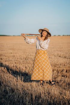 Rural woman plays on wooden flute - ukrainian telenka, tylynka in wheat field. Folk music, sopilka concept. Musical instrument. Musician in traditional embroidered shirt - Vyshyvanka. Quality photo