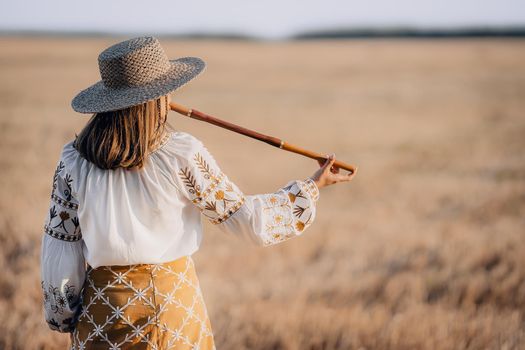 Woman playing on woodwind wooden flute - ukrainian telenka or tylynka in wheat field. Folk music concept. Musical instrument. Musician in traditional embroidered shirt - Vyshyvanka. High quality photo