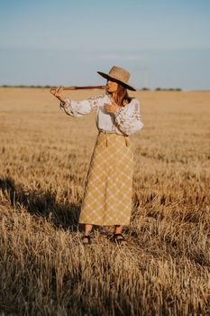 Woman playing on woodwind wooden flute - ukrainian telenka or tylynka in wheat field. Folk music concept. Musical instrument. Musician in traditional embroidered shirt - Vyshyvanka. High quality photo