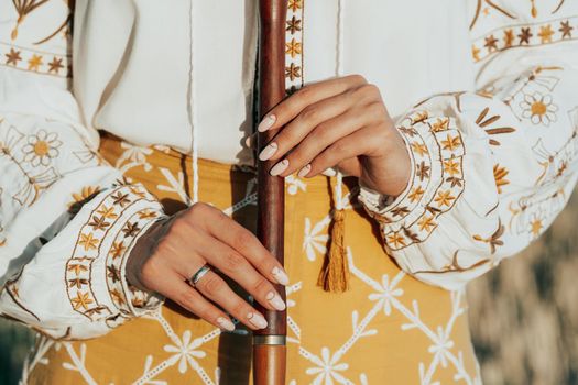 Woman holding woodwind wooden flute - ukrainian telenka or tylynka. Folk music concept. Musical instrument. Musician in traditional embroidered shirt - Vyshyvanka. High quality photo