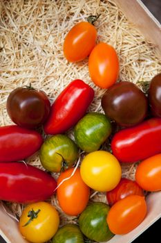 Various tomatoes in a wooden crate on a market stall