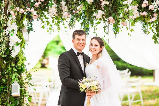 Wedding couple under the flower arch at the wedding ceremony outdoors in the park