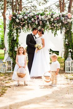 Bride and groom are smiling after wedding ceremony. Adorable children with flying rose petals in baskets
