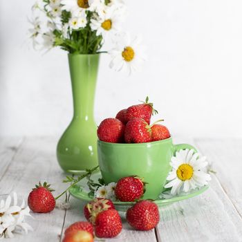 ripe strawberries from the garden in a green mug with white chamomile, fruity summer still life, close-up. High quality photo