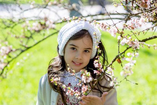 Portrait of a little girl in the flowering branches of a spring tree in sunny day . Close up