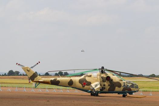 Russian military mi-24a gunship attack helicopter parked at airfield with airplane flying past
