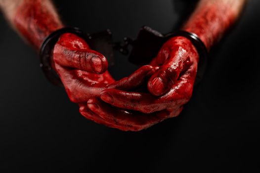 Close-up of male bloody handcuffed hands on a black background