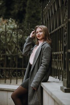 young beautiful girl posing on the autumn street. Dressed in a stylish gray coat, knitted pink sweater and skirt. small stylish handbag