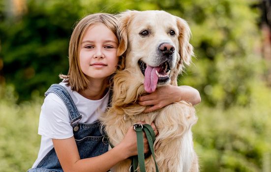 Preteen girl petting golden retriever dog at street. Female child kid with purebred dog labrador sits on ground.