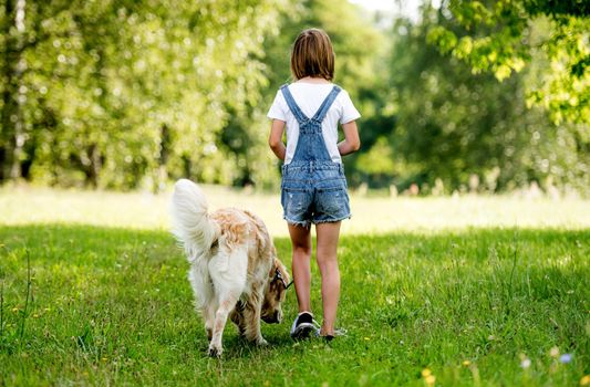 Rear view of a little girl walking dog on flowering meadow. Back view