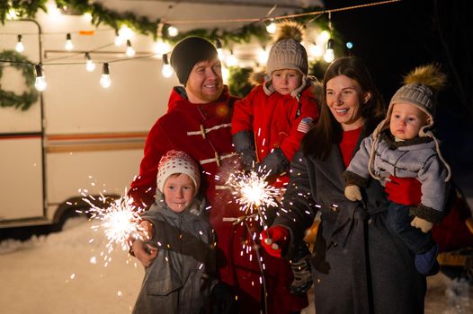 Happy family celebrates christmas in nature and holds sparklers. Parents with three sons travels in a van
