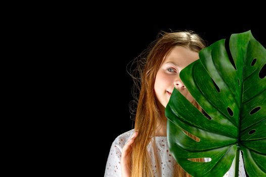 Personal care, cosmetology concept for young teenagers. Portrait of young girl with healthy glow skin holds green monstera leaf and covers part of her face.