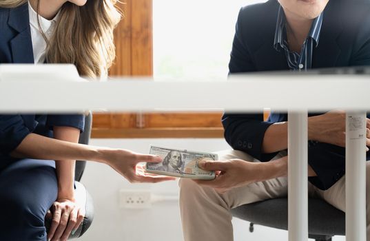 A businessman secretly passing money or bribe under a table to his partner. Business corruption concept