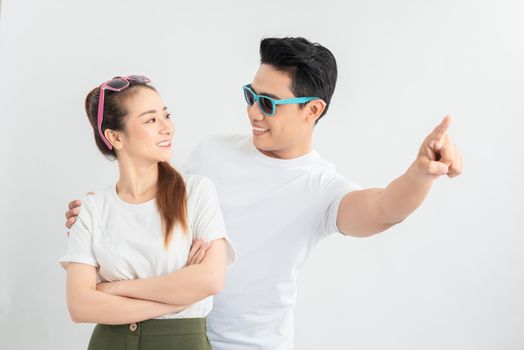 happy asian man hugging smiling girlfriend while pointing with finger isolated on white