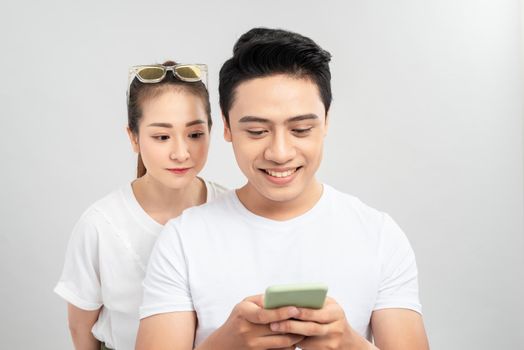 Attractive suspicious young couple standing isolated over white background, using mobile phone