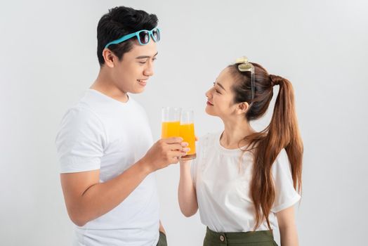 Beautiful young couple standing isolated over white background, holding glasses with orange juice