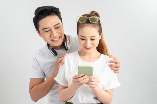 Asian couple using smartphone / mobile handset, standing isolated over white background