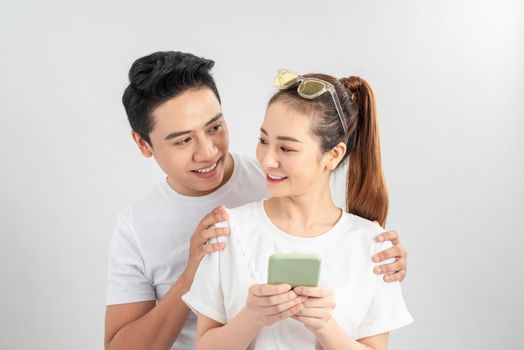 Curious boyfriend is spying his lovers smartphone. They are wearing casual shirts, standing isolated on white background