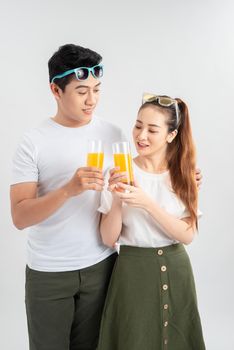 Beautiful young couple standing isolated over white background, holding glasses with orange juice