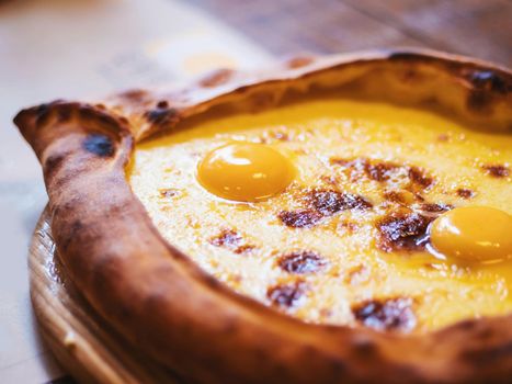 Adjarian khachapuri in restaurant. Open bread pie with cheese and egg yolk. Yummy georgian cuisine.