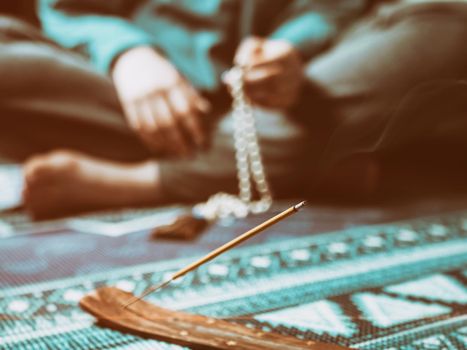 Concentrated woman praying with wooden rosary mala beads. Close up, focus on incense stick. Retro vintage filter.