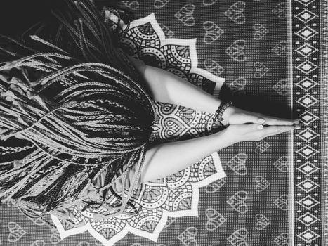 Concentrated woman with blue african braids praying with wooden rosary mala beads. Namaste. Close up hands on yoga mat with mandala. Top view.