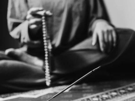 Concentrated woman praying with wooden rosary mala beads. Close up, focus on incense stick