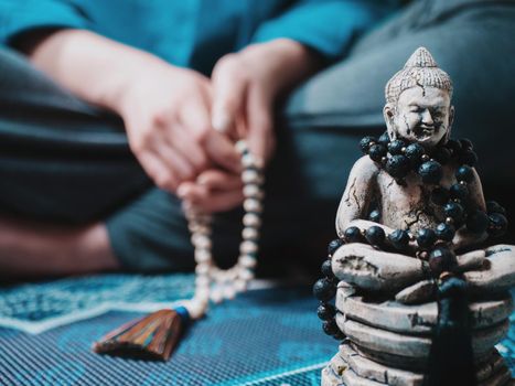 Concentrated woman praying with wooden rosary mala beads. Namaste. Close up statue of Buddha.