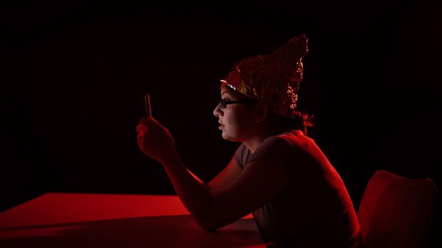 Paranoid caucasian woman using smartphone wearing tinfoil hat. Conspiracy theory