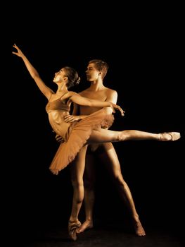 Professional, emotional ballet dancers on dark scene performed by sexual couple with golden body art.Shining gold skin.Pair depicts love and passion on stage.