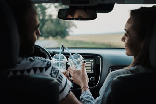 Back view on middle-aged couple sitting inside car and drinking coffee, man and woman enjoying road trip